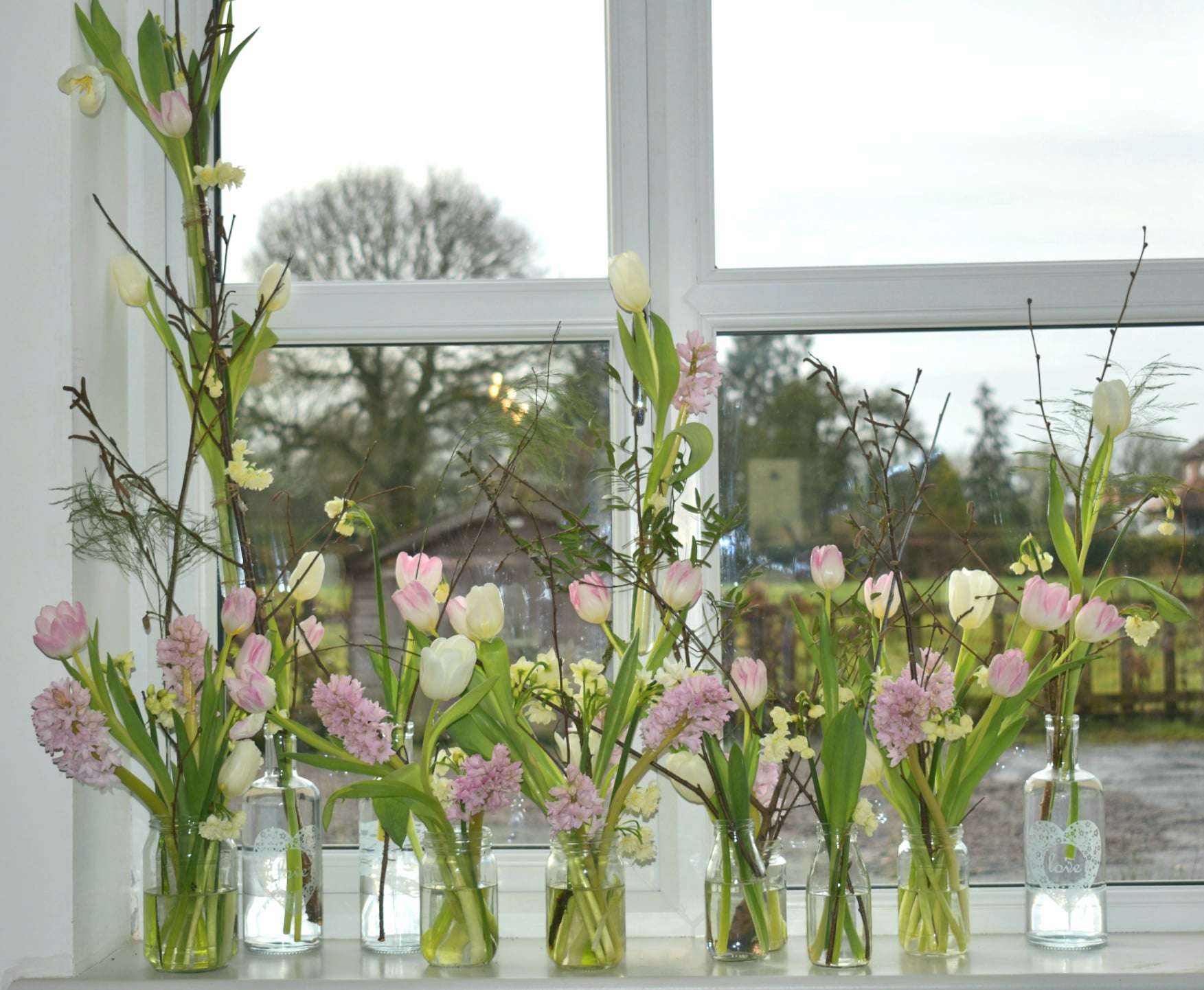 Collection of spring tulip and hyacinth arrangements in clear glass bottles on a bright windowsill