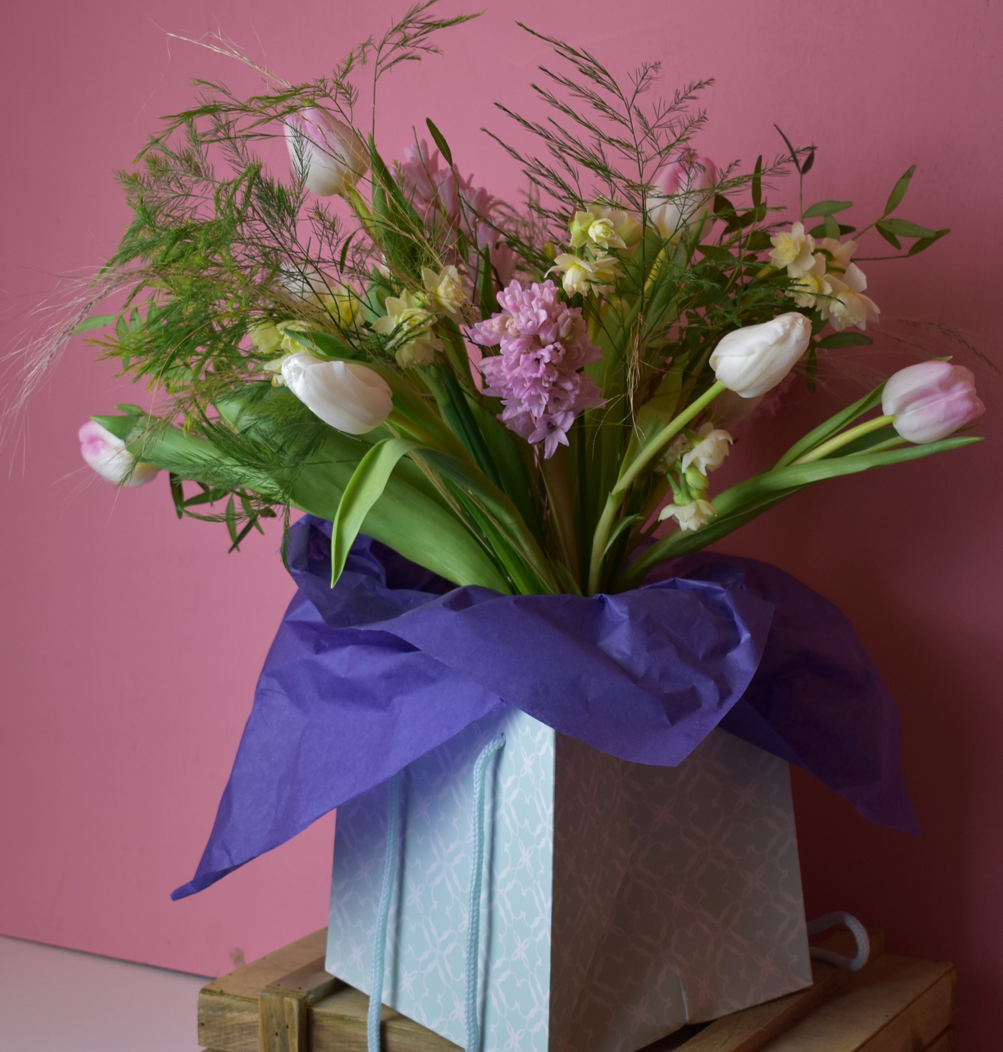 Spring bouquet of pastel tulips and hyacinths with fern fronds wrapped in purple tissue paper