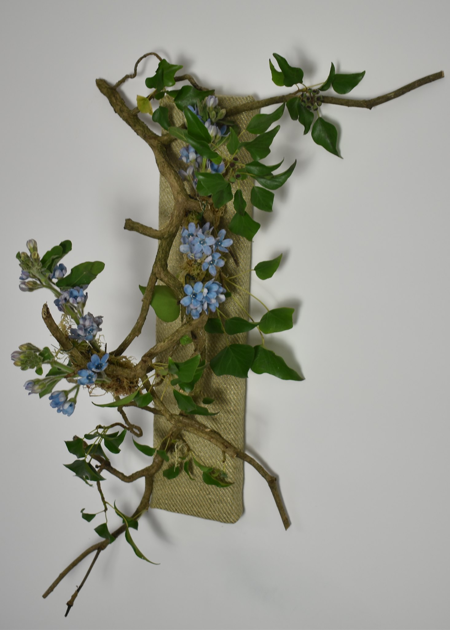 Artistic floral wall piece with blue flowers entwined on natural branches against a white background