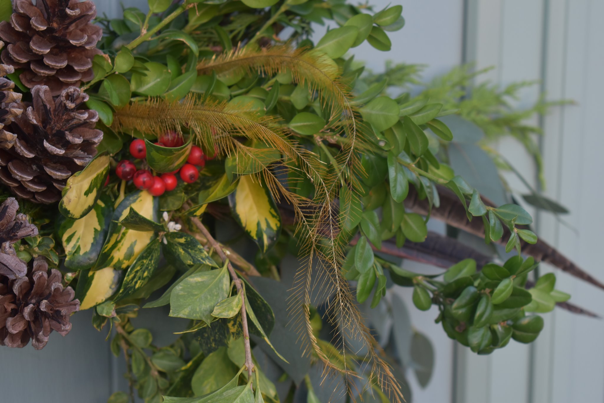 Festive wreath detail with holly berries, golden grasses, pinecones, and lush boxwood greenery
