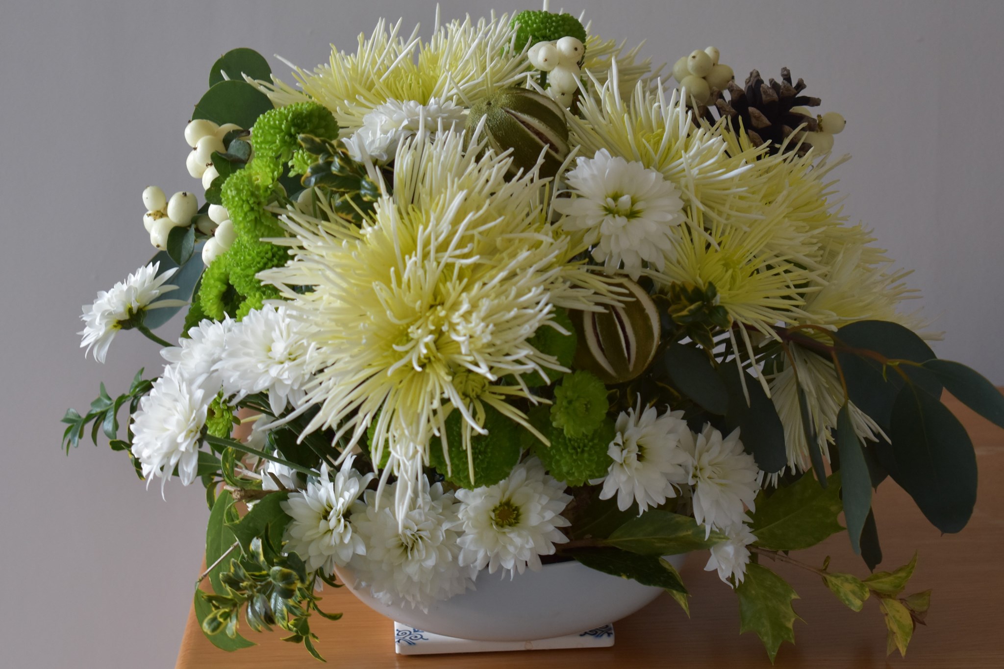 Elegant white and green chrysanthemum arrangement with eucalyptus and berries in a ceramic bowl