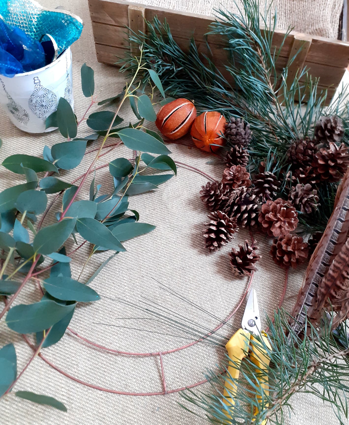 Behind the scenes --- wreath-making supplies laid out: eucalyptus branches, pinecones, dried oranges, and a wire frame