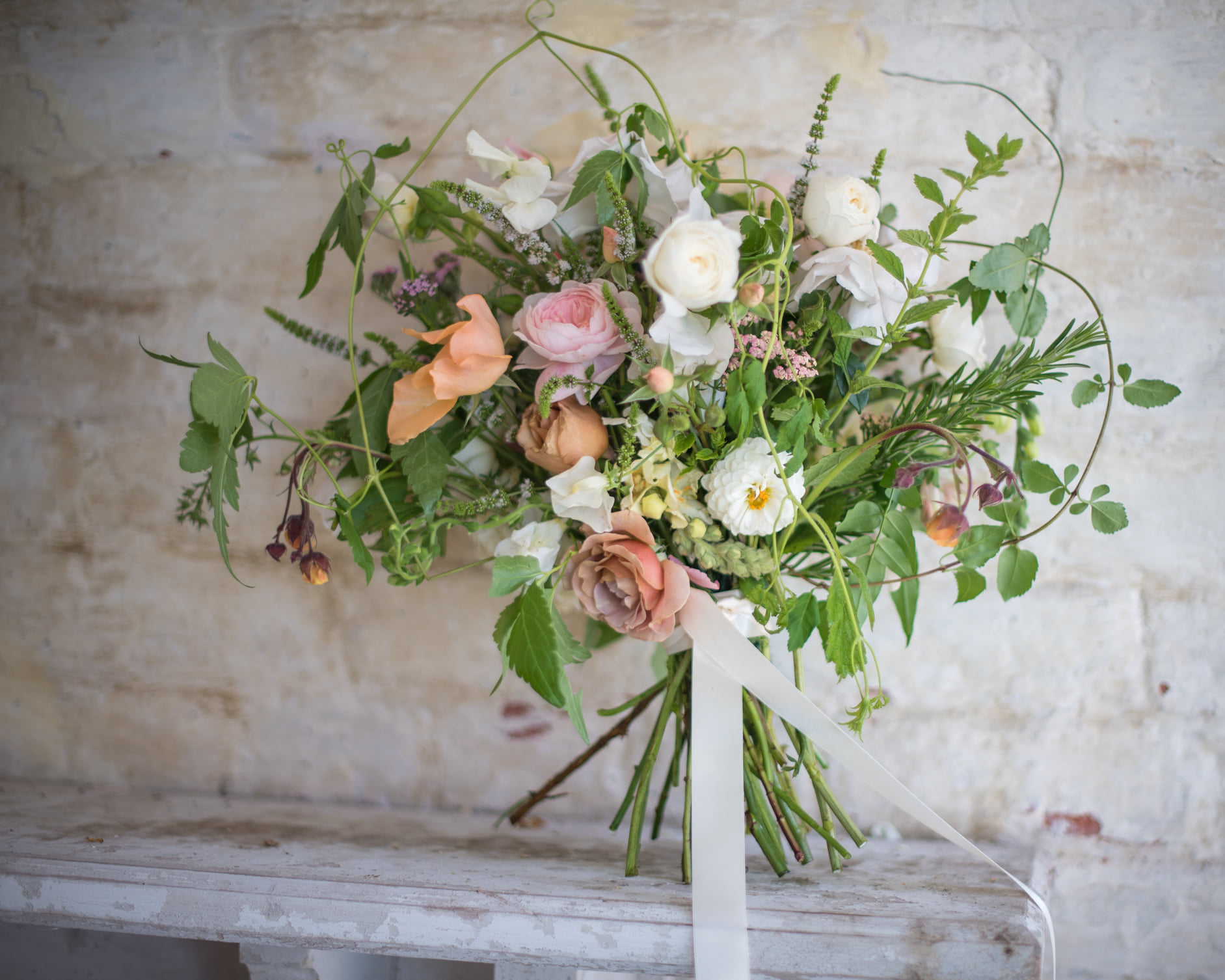 Lush hand-tied bouquet of roses, white blooms, and trailing greenery against a textured stone wall